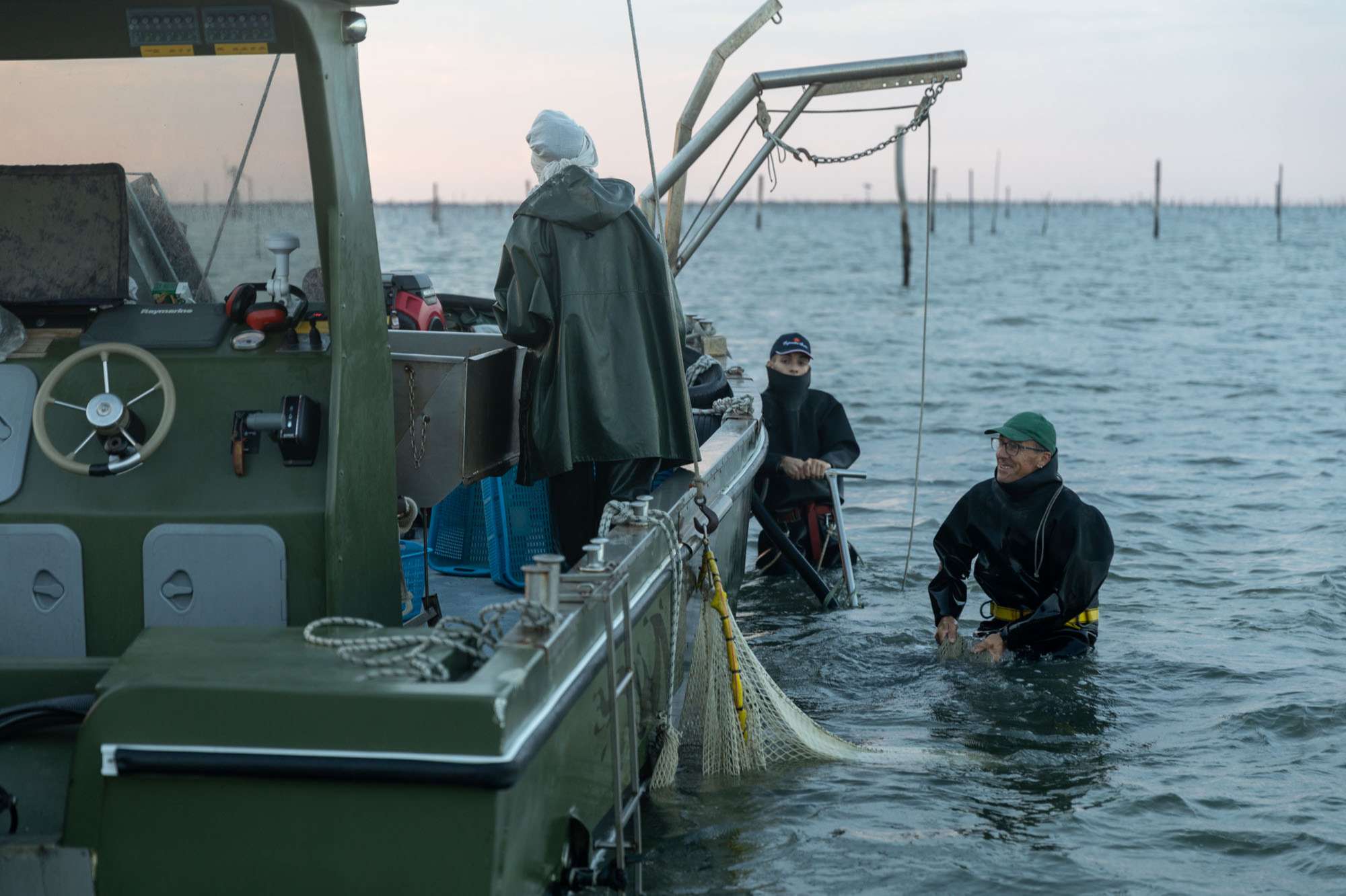 Fase di pesca. Pescatori con raschia e reti raccolgono le vongole seminate e le separano per taglia con setacciatore automatico.
