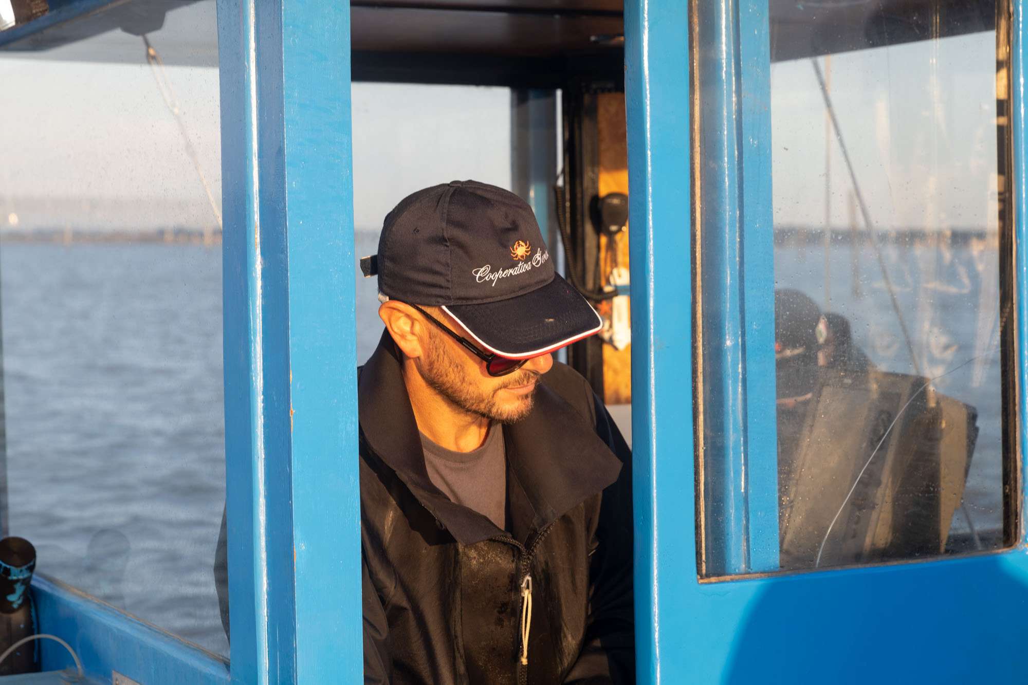 Pescatore in cabina di guida con cappellino Cooperativa Gorino.